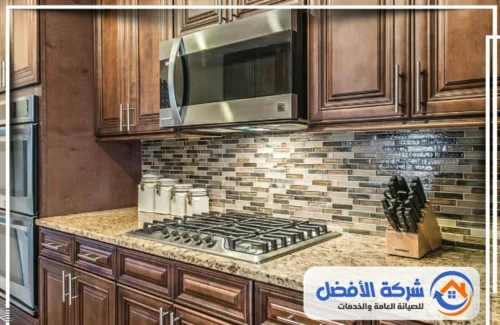 تصميم مطابخ خشمنيوم بمكة مطبخ كلاسيكي بأثاث خشبي داكن، سطح عمل رخامي، وبلاط فسيفسائي خلفي.