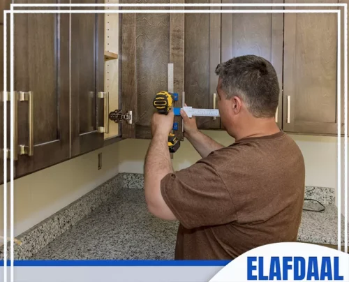 تركيب مطابخ المنيوم جدة 0594257100 الأفضل فني يركب مقابض ذهبية جديدة على خزائن مطبخ بنية غامقة باستخدام مثقاب كهربائي.