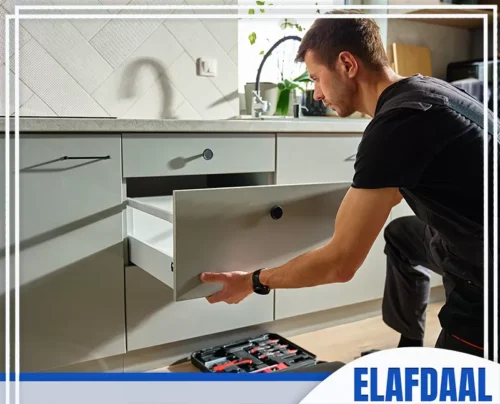 تركيب دولاب مطبخ جدة 0594257100 الأفضل فني يفحص درجًا مفتوحًا لوحدة مطبخ رمادية، وبجانبه صندوق أدوات الصيانة.