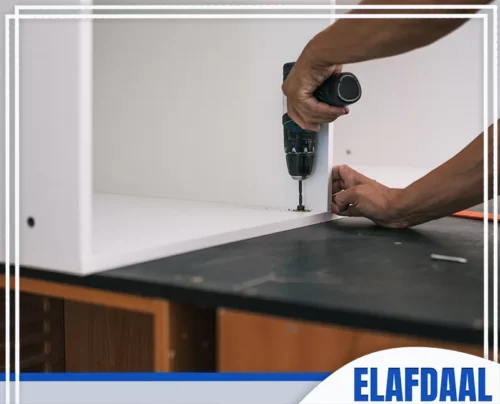 ورشة مطابخ المنيوم بجدة 0594257100 الأفضل فني يستخدم مثقاب كهربائي لتثبيت وربط أجزاء وحدة المطبخ الخشبية البيضاء أثناء التركيب.