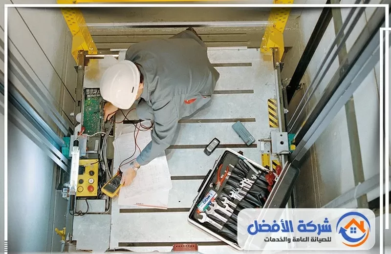 فني صيانة مصاعد يرتدي خوذة أمان ويجري فحصًا للأجزاء الكهربائية والميكانيكية داخل كابينة المصعد.