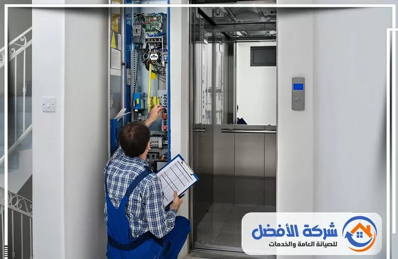 فني صيانة مصاعد يفحص لوحة التحكم والدوائر الكهربائية بجانب كابينة المصعد لإجراء أعمال الفحص والصيانة.