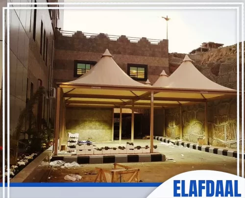 مؤسسة مظلات بالرياض 0569607972 شركة الافضل مظلة خيامية أنيقة ذات تصميم مخروطي متعدد القمم، ترتكز على إطار خشبي أو معدني مطلي بلون الخشب الفاتح.