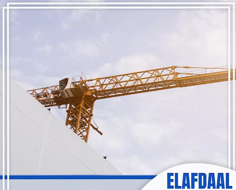 الصورة توضح رافعة برجية كبيرة بجوار مبنى قيد الإنشاء، تستخدم لرفع مواد ومعدات البناء الثقيلة داخل موقع العمل.